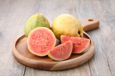 Yemek masasındaki tahta kesme tahtasının üzerinde kırmızı guava dilimleri.