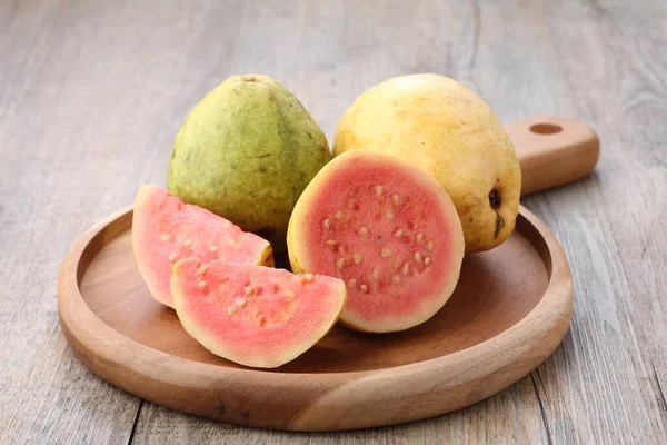 Yemek masasındaki tahta kesme tahtasının üzerinde kırmızı guava dilimleri.