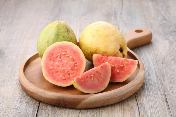 Yemek masasındaki tahta kesme tahtasının üzerinde kırmızı guava dilimleri.