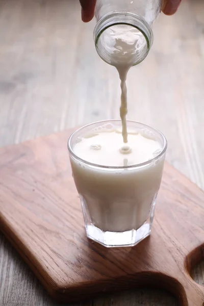 把牛奶倒入木制桌子上的杯子里 — 图库照片