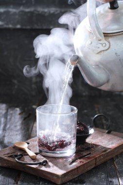 Çaydanlıklı çay fincanı ve ahşap arka planda bir bardak su.