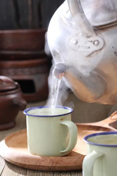 Tahta bir masada çay seti, bir çaydanlık ve bir fincan sıcak çay. 