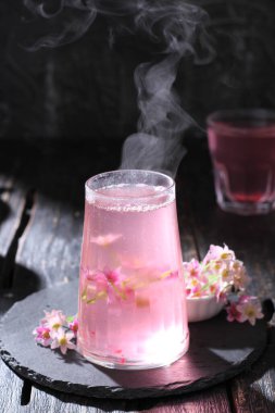 Tahta bir masada buzlu, çay ve çiçekli sıcak bir içecek..