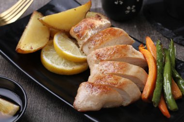 Izgara tavuk göğsü ve siyah tabakta sebzeler.