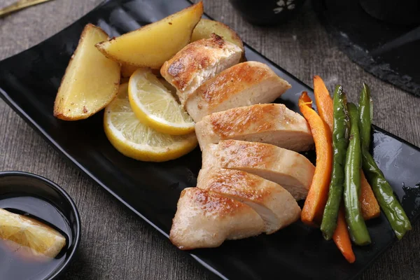 Patatesli ızgara tavuk ve gri taş masada limon.