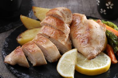 Siyah tabakta patates ve sebzeli ızgara tavuk.