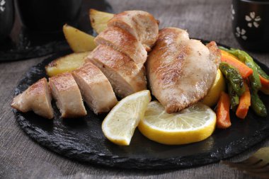 Izgara tavuk göğsü ve siyah tabakta sebze.