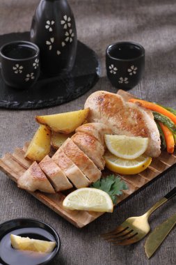 Limonlu ızgara tavuk göğsü ve siyah tabakta sebze.