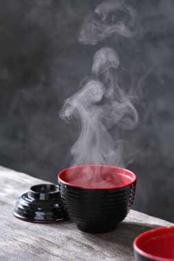 Bir kase sıcak siyah çay ya da dumanlı buhar ve koyu bir arka planda..