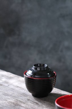 Ahşap masada kırmızı çay fincanı olan siyah seramik kase.