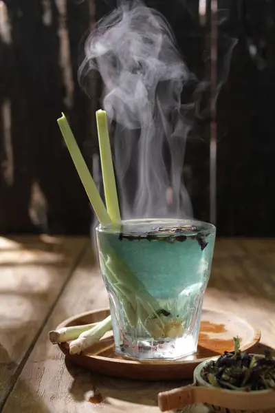 a glass of green tea with ice cubes and smoke on a wooden table