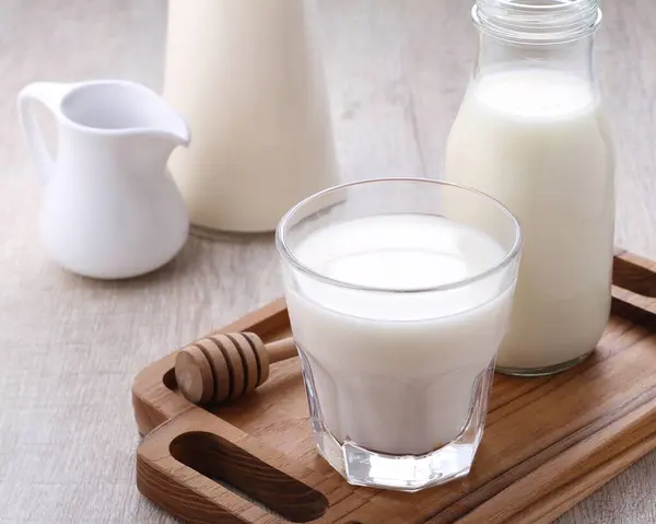 glass of milk and fresh milk in a wooden tray with a jug and a straw.