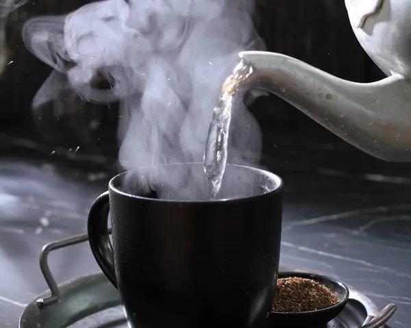 a cup of tea with smoke and a black spoon on a black background