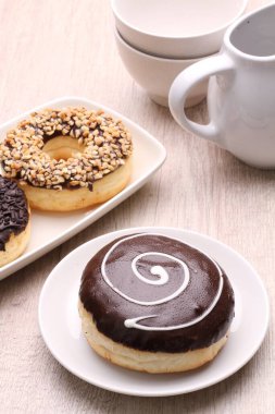 Beyaz ahşap masada bir fincan kahve ve çikolata parçalı donut. Tatlı hamur işleri