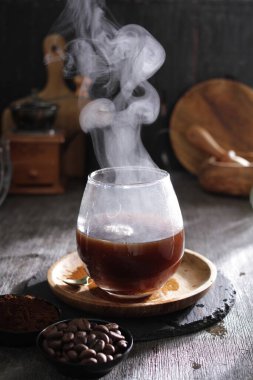 Kahve fincanı ve sıcak kahve çekirdekleri ahşap masada.