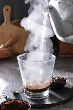 Bir fincana su döken dumanı tüten bir çaydanlık.