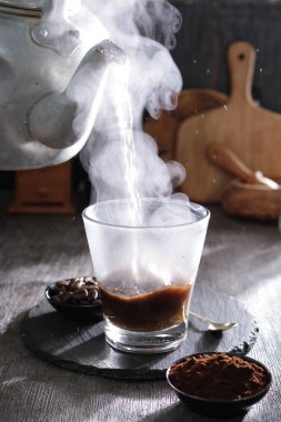 Bir kaşık ve kaşıkla masanın üzerinde duran dumanı tüten bir fincan kahve.