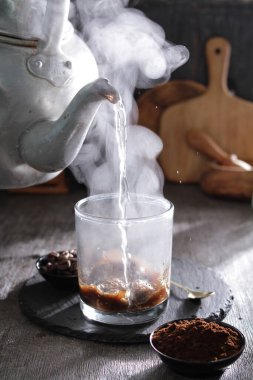 bir çaydanlık bardağa su döküyor.