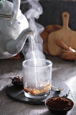 bir çaydanlık bardağa su döküyor.