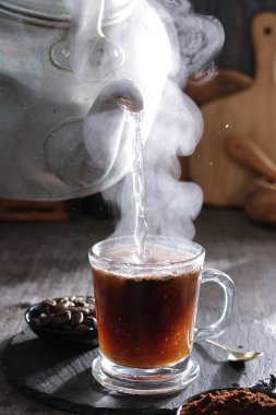 Buharı tüten bir çay fincanı kaşık ve kaşıkla masada dinleniyor.