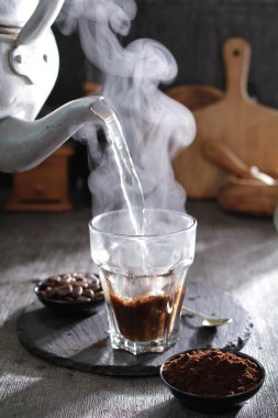 bir çaydanlık bardağa su döküyor.