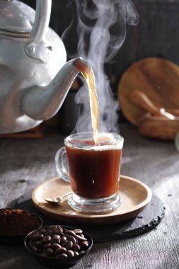 Sıcak kahveyi fincana döken bir çaydanlık.