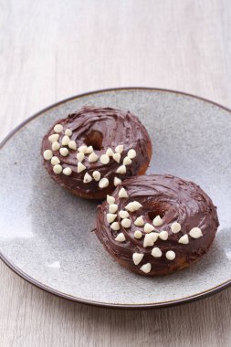 iki çikolatalı çörek, tabakta beyaz serpiştirilmiş.