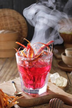 Bir bardak kırmızı sıvı kaşık ve bir kaşık kesme tahtasının üzerinde dinleniyor.