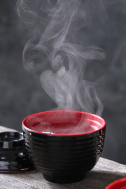 Buharlı bir kase sıcak siyah çay ve koyu bir masada kırmızı çay.