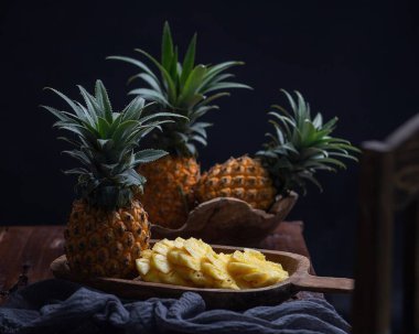 Tahta bir masada siyah bir tabakta taze ananas ve portakal.