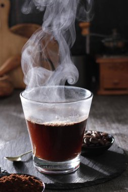 Siyah arka planda bir fincan kahve ve kahve çekirdeği. dumandan buhar çıkıyor.