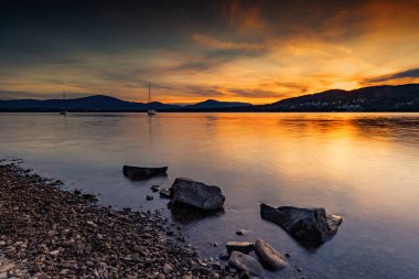 Dağlı renkli bir gün batımı ve arkasında dağlar olan bir göl.