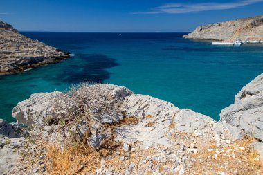 Kayalık kıyı şeridi ve açık bir gökyüzü altında uzak dağları olan deniz burnu, Yunan Adaları