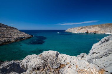 Kayalık kıyı şeridi ve açık bir gökyüzü altında uzak dağları olan deniz burnu, Yunan Adaları