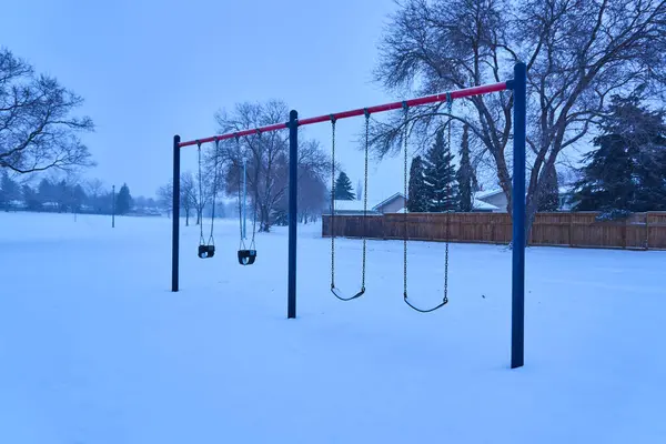 Explore the magic of a small park blanketed in snow, where swings and playground equipment are adorned in white, creating a magical and serene winter scene.