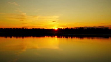 Sakin bir gölün üzerinde gün batımının güzel 4K görüntüleri. Suyun üzerinde parlak renkler yansıyor..