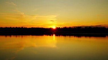 Sakin bir gölün üzerinde gün batımının güzel 4K görüntüleri. Suyun üzerinde parlak renkler yansıyor..