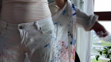 Kadın sanatçı iş kıyafetlerini giyip kendini yaratmaya hazırlanıyor. Renkli kırmızı ve mavi boya serpiştirilmiş beyaz gömlekli bir ressam. Yüksek kalite 4K görüntü