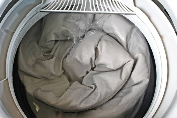 stock image Roll up the duvet and put it in the washing machine.For the presentation of the washing machine.