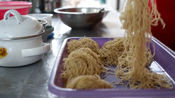 stock image a seller preaparing a dry noddle on a purple tray.