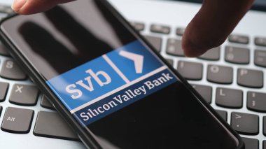 Hand want to grab smartphone with Silicon Valley Bank logo. Acquisition illustration. Jakarta, 21 March 2023.