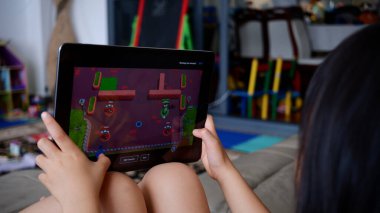 Oturma odasındaki kanepede iPad 'de oyun oynayan küçük bir kız. Jakarta, 17 Temmuz 2023