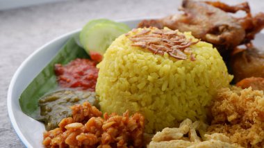 Beyaz tabakta Nasi Kuning veya Sarı pirinç. Geleneksel kızarmış tavuk, tofu, tempeh ve ezilmiş patates ile birlikte sarı pirinç. Endonezya yemekleri.