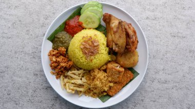 Nasi Kuning or Yellow rice on a white plate. Yellow rice with traditional fried chicken, tofu, tempeh, and smashed potato. Indonesia food. clipart