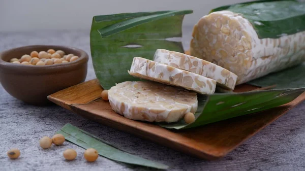 Raw tempeh ya da tempe mentah. Tempeh ahşap tabakta dilimler. Kahverengi seramik kasede çiğ soya çekirdeği. Tempe aslında Endonezya 'dan mayalanmış soya ürünüdür..