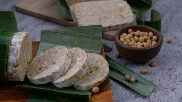 Raw tempeh ya da tempe mentah. Tempeh ahşap tabakta dilimler. Kahverengi seramik kasede çiğ soya çekirdeği. Tempe aslında Endonezya 'dan mayalanmış soya ürünüdür..