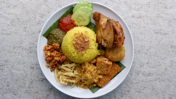 Nasi Kuning or Yellow rice on a white plate. Yellow rice with traditional fried chicken, tofu, tempeh, and smashed potato. Indonesia food.