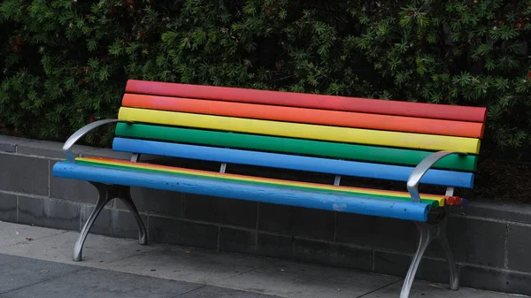 A colorfull rainbow color chair in a park.