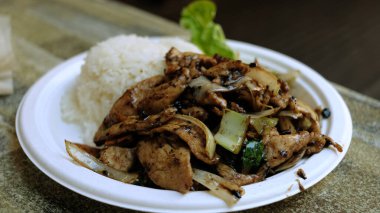 Tahta bir masada beyaz plastik bir tabakta soğanlı ve pirinçli siyah biberli tavuk..