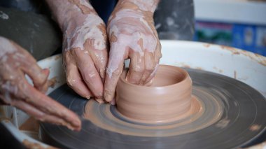 Bir eğitmen öğrencisine tekerlek fırlatarak çömlek yapmayı öğretiyor..